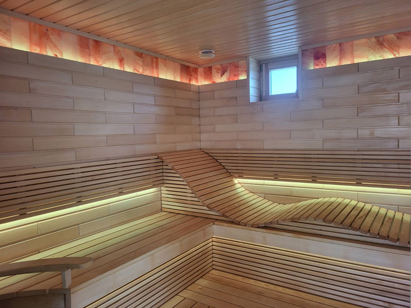 Sauna wykonana z jasnego drewna, z falistą ławką i oświetleniem LED.